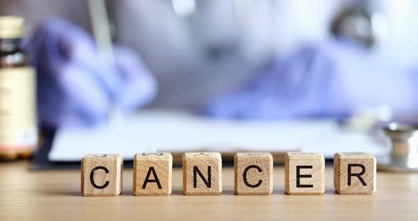 Doctor Filling Out Medical Paperwork on Background of Wooden Cubes with Word Cancer Closeup  Movie