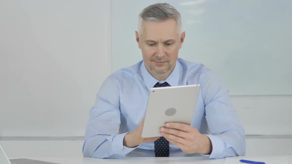 Senior Businessman Browsing Internet on Tablet in Office