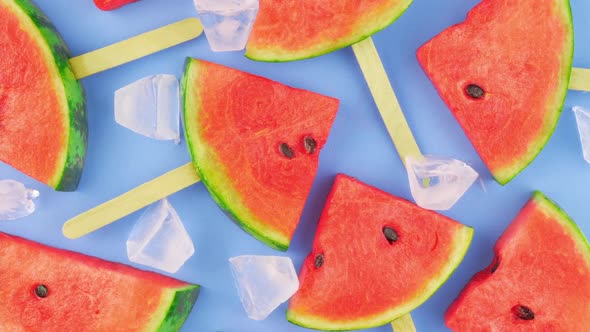 Watermelon slices on sticks with ice cubes. Fresh watermelon popsicles on blue background.