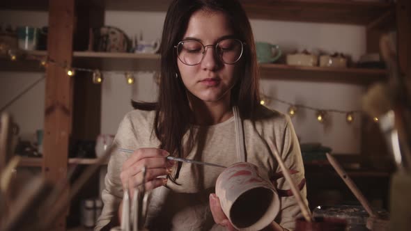 Young Woman in Art Studio Coloring Ceramic Product with a Brush Then Looks in the Camera