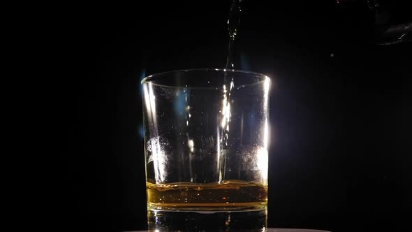 Closeup of Whiskey Pouring Into a Glass That Rotates on a Black Background