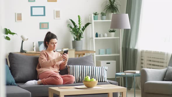 Young Woman Sitting on Couch and Using Smartphone at Home