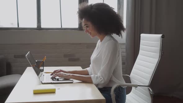 Concentrated Biracial Girl Uses Laptop for Work in the Modern Office. Beautiful Young Woman Types on
