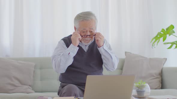 elderly handsome asian man wear glasses sitting on sofa using computer laptop and smile