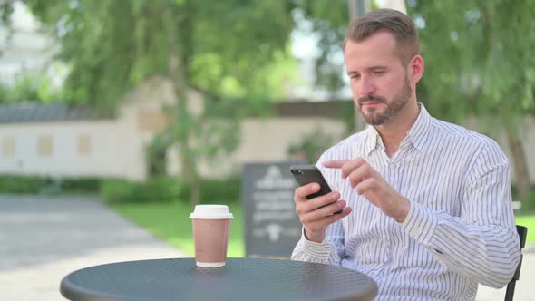 Middle Aged Man Celebrating Success on Smartphone in Outdoor Cafe