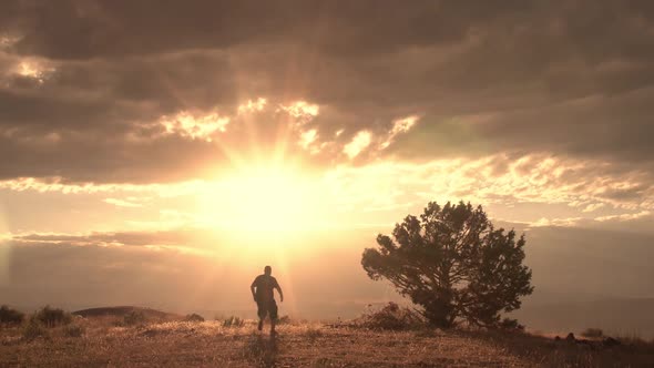 Person running and stopping on hilltop viewing landscape