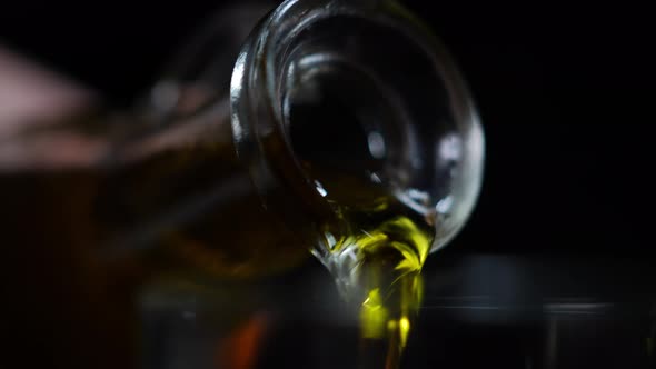 Closeup Shiny Golden Oil Pouring From Glass Jar in Transparent Bowl at Black Background