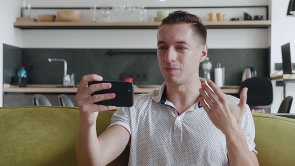 Smiling Young Man Making Video Call While Sitting on a Couch at Home. Portrait of Male Doing a Video