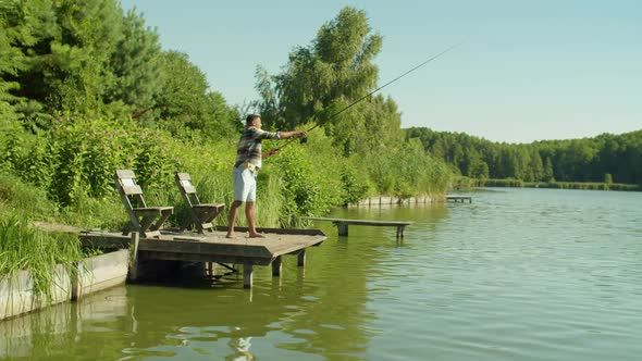 Relaxed African American Fisherman with Rod Enjoying Angling From Jetty on Pond