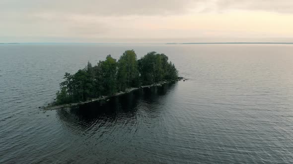 Aerial rising, tilt view of a small island, in the middle of a restless, wavy sea, on a dark, cloudy