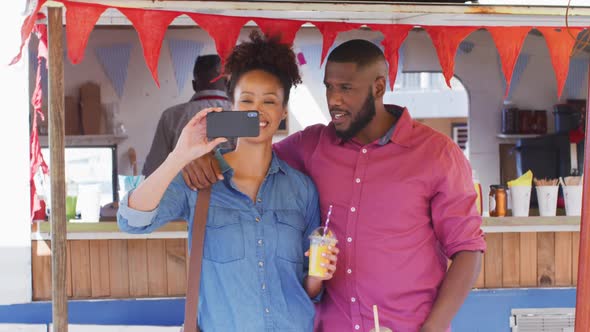 African american couple holding smoothies smiling while taking a selfie at the food truck