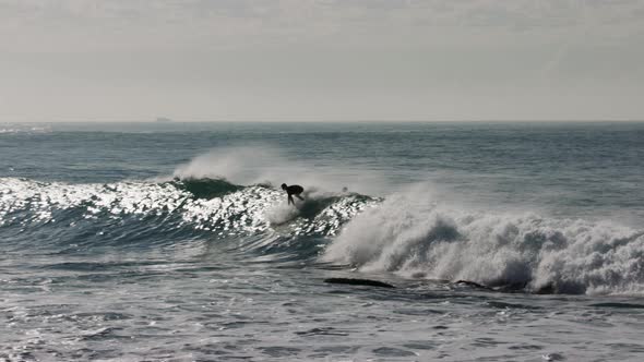 A surfer stands up and gets ahead of a strong wave breaking on a shallow rocky break near the coast