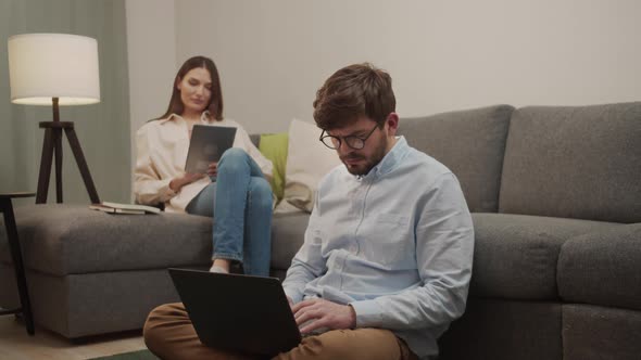 A European Man and Woman Looking at Gadgets Sitting at Home on the Couch