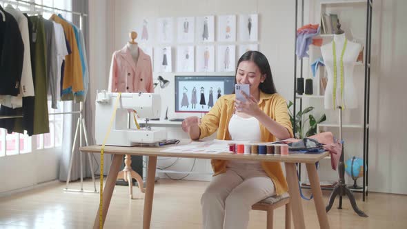 Female Designer With Sewing Machine Looking At The Paper In Hand And Comparing It On Smartphone