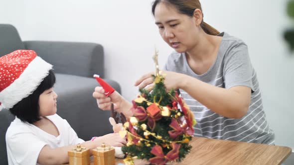 Happy lovely Asian girl decorating ornament on Christmas tree with mother.