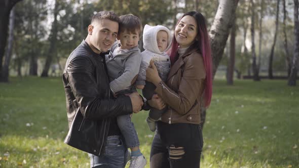 Portrait of Positive Caucasian Husband and Wife Carrying Sons on Hands and Smiling at Camera