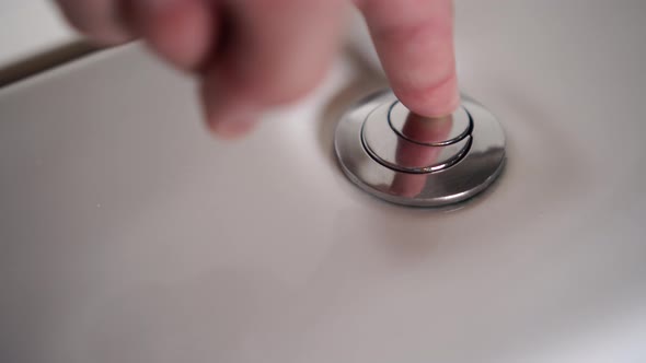 A male hand presses the shiny button of a white ceramic toilet bowl