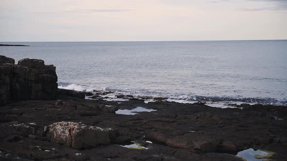 Beautiful waves splashing on the rocky shoreline of Dunstanburgh, England - wide shot