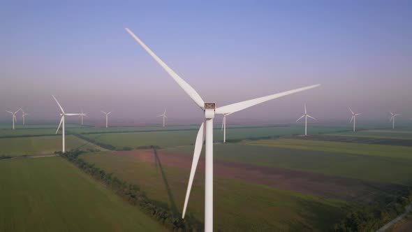 Windmills with rotating wings among green fields. Wind farm for wind energy.