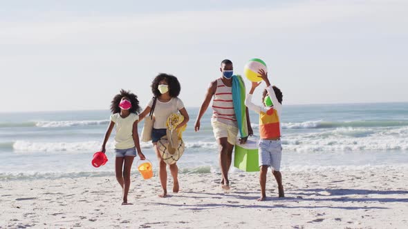 African american parents and their children wearing face masks carrying beach equipment on the beach