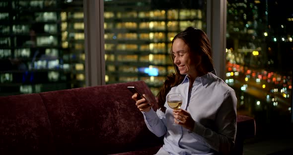 Portrait of a Cheerful Woman in a Shirt Is in the Apartment, She Is Sitting on a Purple Sofa