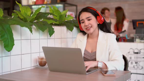 Asian woman is working with laptop in cafe enjoying listen music in headphones singing having fun 