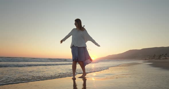 Happy Woman Having Fun on the Ocean Shore with Wind Blowing Her Hair and Dress