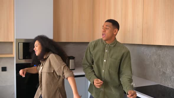 Happy AfricanAmerican Couple Dancing in the Kitchen Singing While Cooking Breakfast