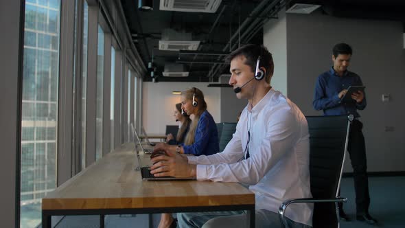 Man in Shirt Using a Headset with Laptop While Working in Call Center Office