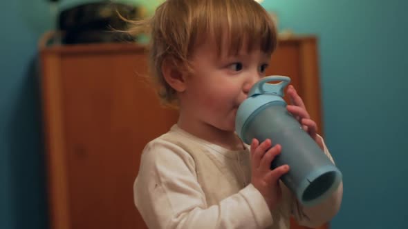 A Cute Chubby Toddler Drinking Smoothie Put In A Blue Container While Watching His Parents Beside Hi