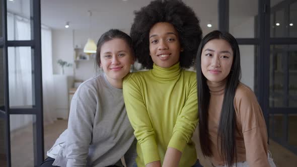Three Charming Multiethnic Young Women Posing Indoors Looking at Camera Smiling