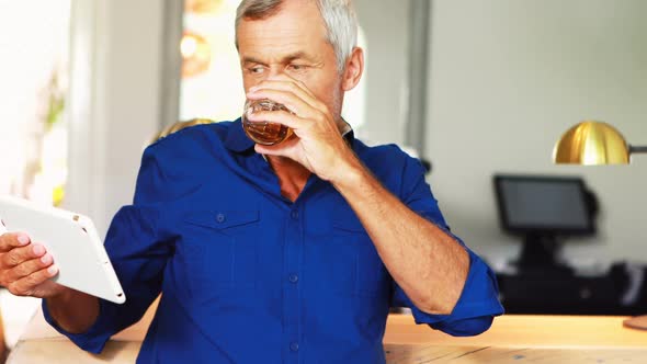 Mature man using digital tablet while having beer