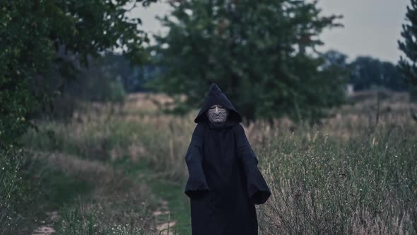 Portrait of scary death in black. Spooky figure in dark mantle with hood coming to camera