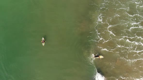 Aerial shot of two female surfers, one catching a wave in southern California