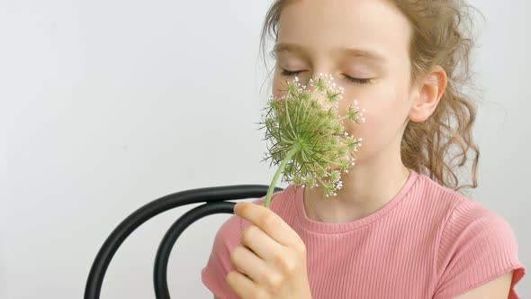 Little Girl is Sitting at Home with Flowers in Hands During Summer Time and Sneezing