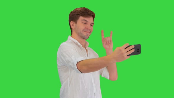 Young Man in Casual White Shirt Taking Selfies on His Phone on a Green Screen, Chroma Key.