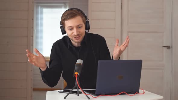 Young hipster man with headphones recording podcast using laptop at home studio