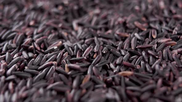 Dry black rice grains fall into a heap with rotation. Macro