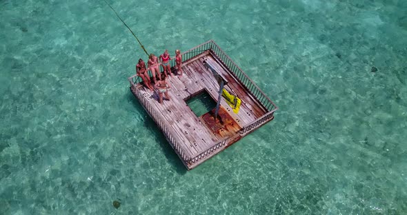 Young women sunbathing over floating platform on crystal emerald waters of lagoon near tropical isla