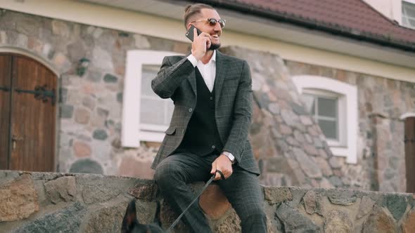 Wealthy Businessman in a Business Suit Is Talking on the Phone and Smiling with a Doberman Dog on a