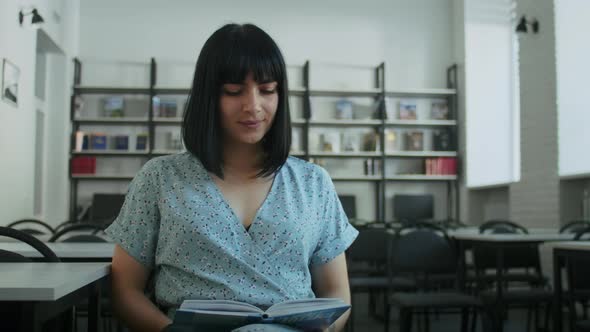 Happy Woman Reads a Book in the Library Chooses Books From the Shelf alt