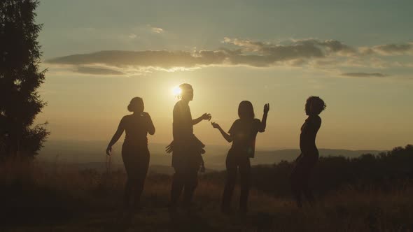 Silhouette of Happy Diverse Friends Enjoying Party and Dancing on Mountain Peak at Sunset