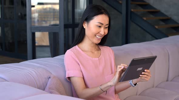A Cheerful Young Asian Woman is Using a Digital Tablet Indoor