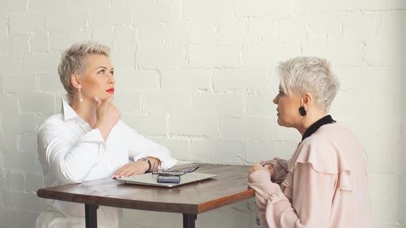 Two Female Senior Collegues Sitting Next To Each Other in an Cafe