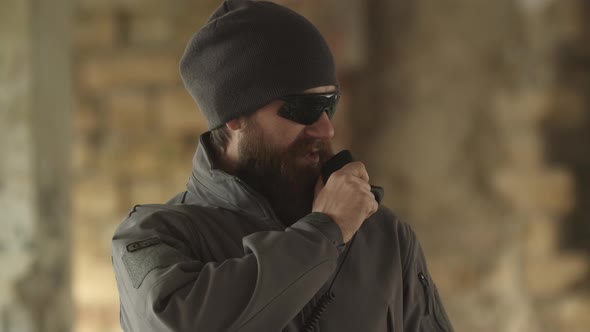 Serious Man in Sunglasses and Military Clothing Speaks on Walkie Talkie Checking Area Patrolling