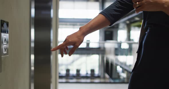 Midsection of caucasian businesswoman pressing button in lift arriving in modern office