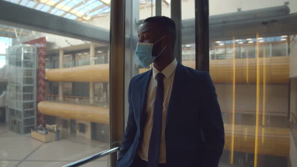 Young Afro-american Businessman in Facial Mask Taking Glass Elevator