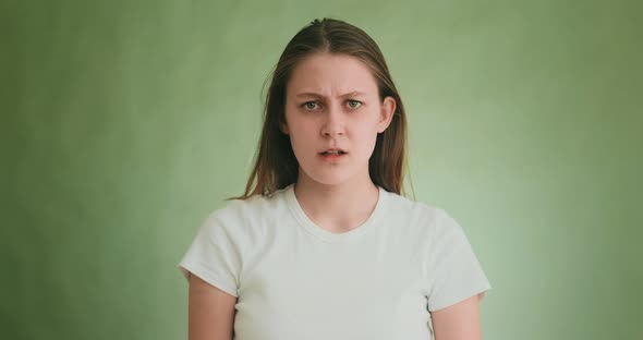 Worried Woman in White Tshirt Looks Into Camera on Green