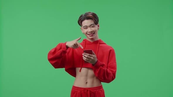 Smiling Asian Transgender Male Use Mobile Phone And Pointing To Smart Phone On Green Screen Studio