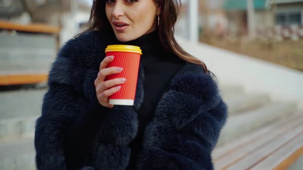 Female hands hold a cup of beverage outdoors.